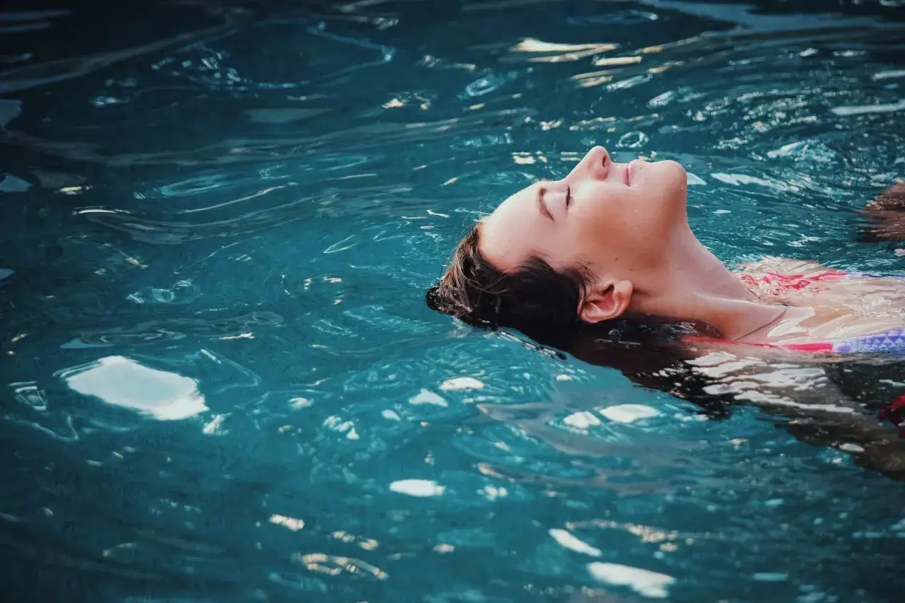 A woman floats serenely in blue water, her face tilted up. She's enjoying the moment, but wonders,