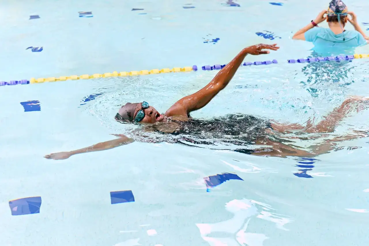 A swimmer practices how to swim laps for beginners, with goggles on and arm extended.