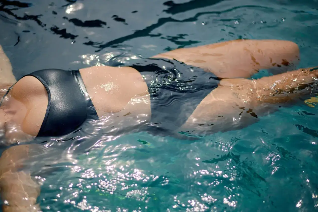 A person floats in a pool, demonstrating how to swim on your period with confidence and comfort.