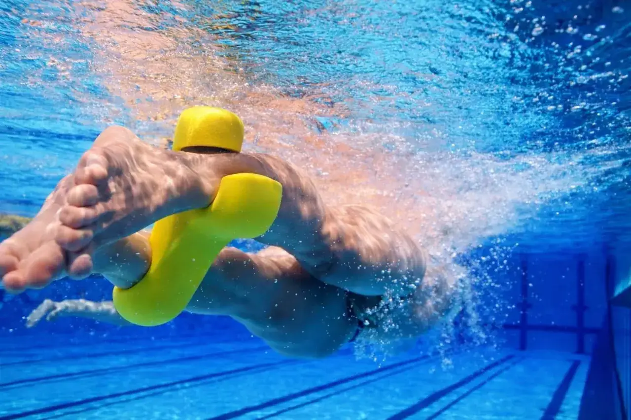 Underwater view of a swimmer's legs and torso, using a yellow flotation device. The water pulls and churns around them.