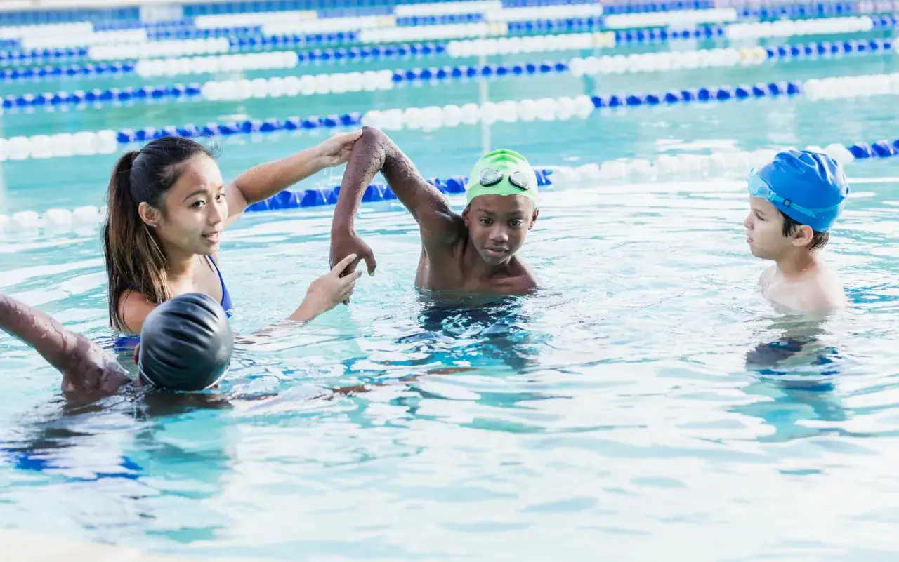 A swim instructor helps young children learn how to swim in a pool.