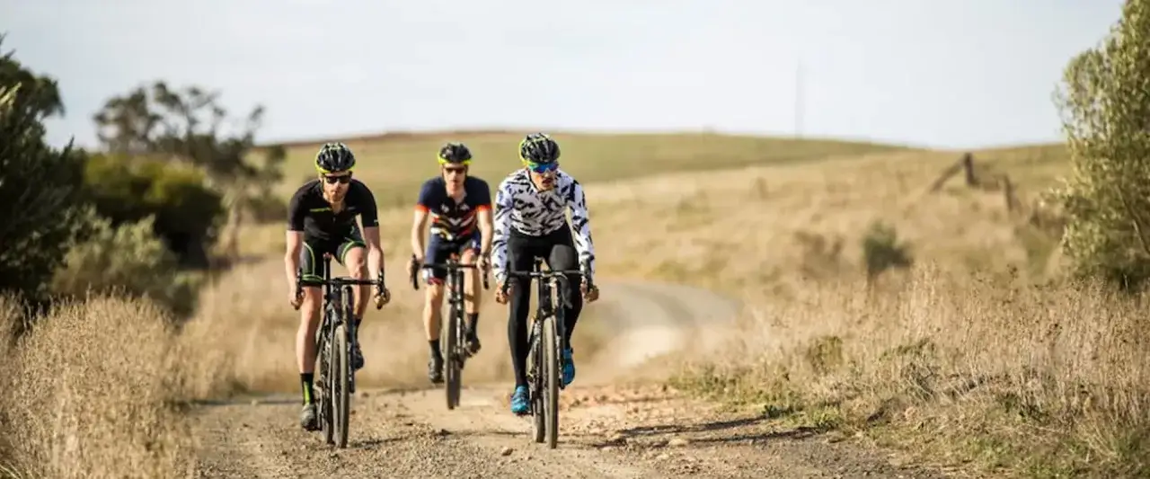 Three cyclists race on a dusty path, tackling a challenging gravel triathlon.