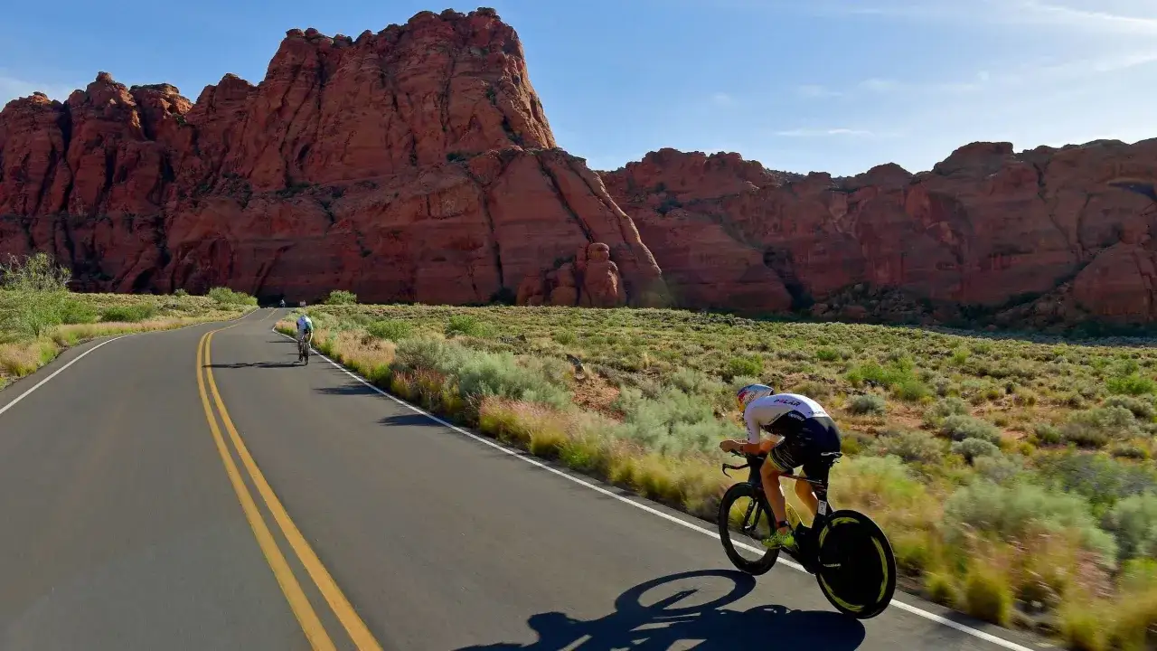 Cyclist races through a desert landscape with red rock formations, part of the Ironman 70.3 St. George course.