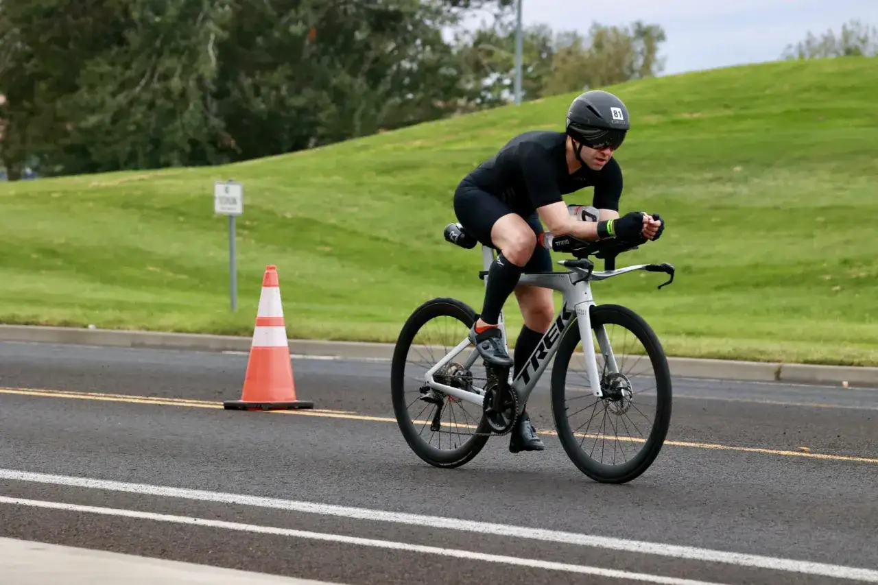 Athlete competes in a road triathlon, cycling intensely on a paved course with a grassy hill in the background.