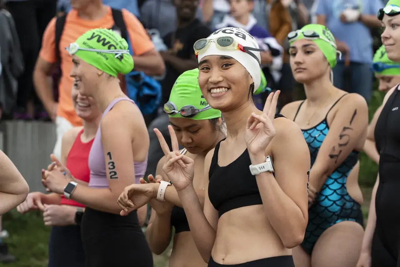 Smiling women in swim caps and goggles ready for a womens triathlon. One gives a peace sign.