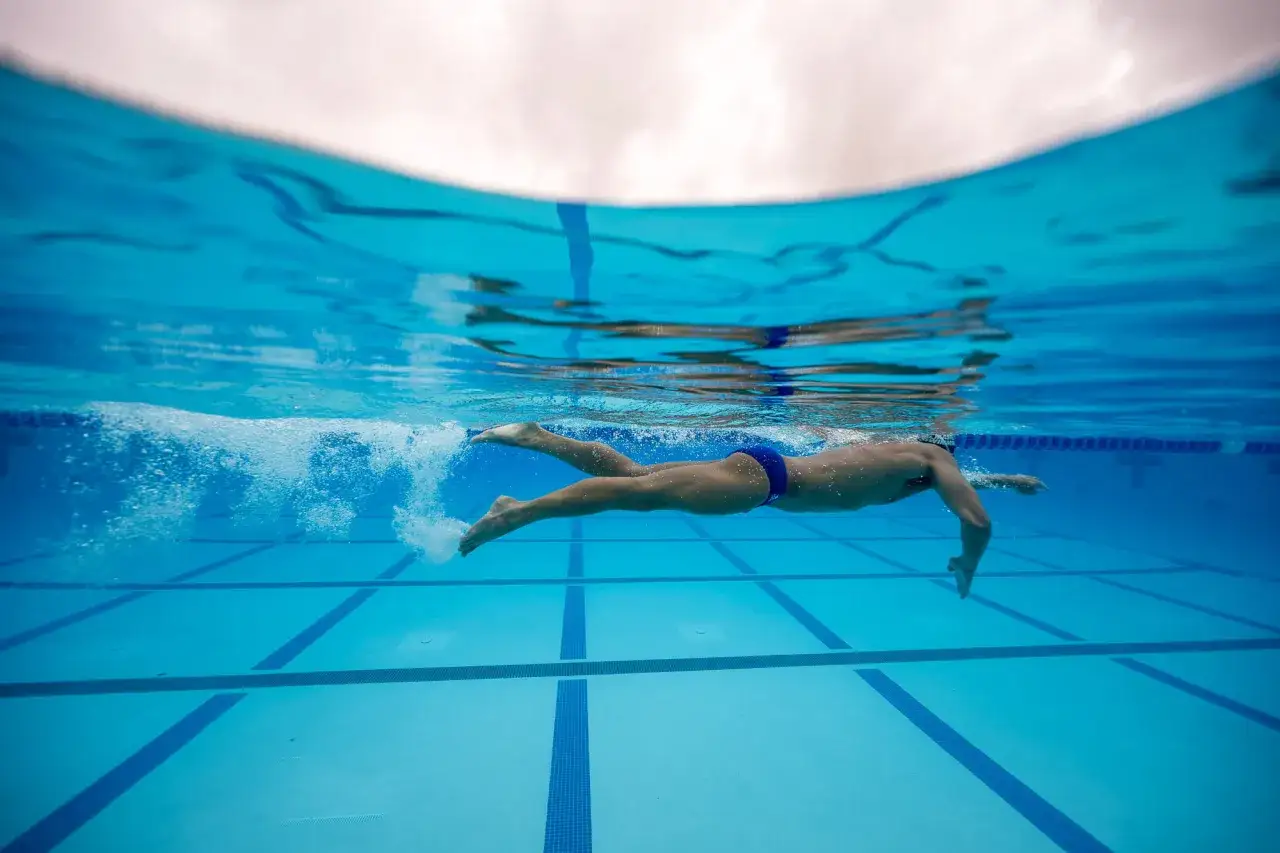 A swimmer propels through the blue water, their powerful leg kicking creating a trail of bubbles.