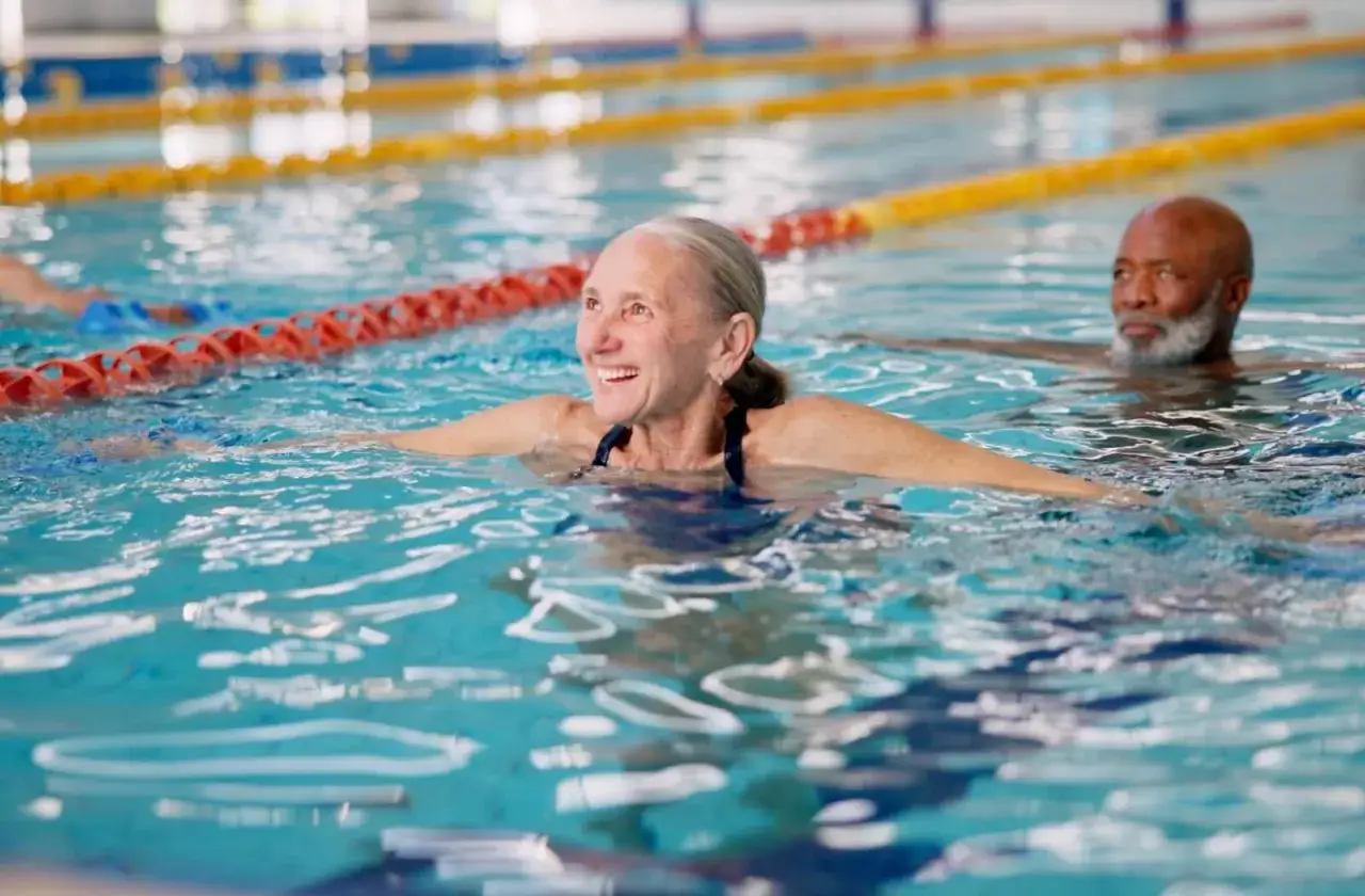 Smiling seniors enjoy swim lessons in a pool, with lane markers visible.
