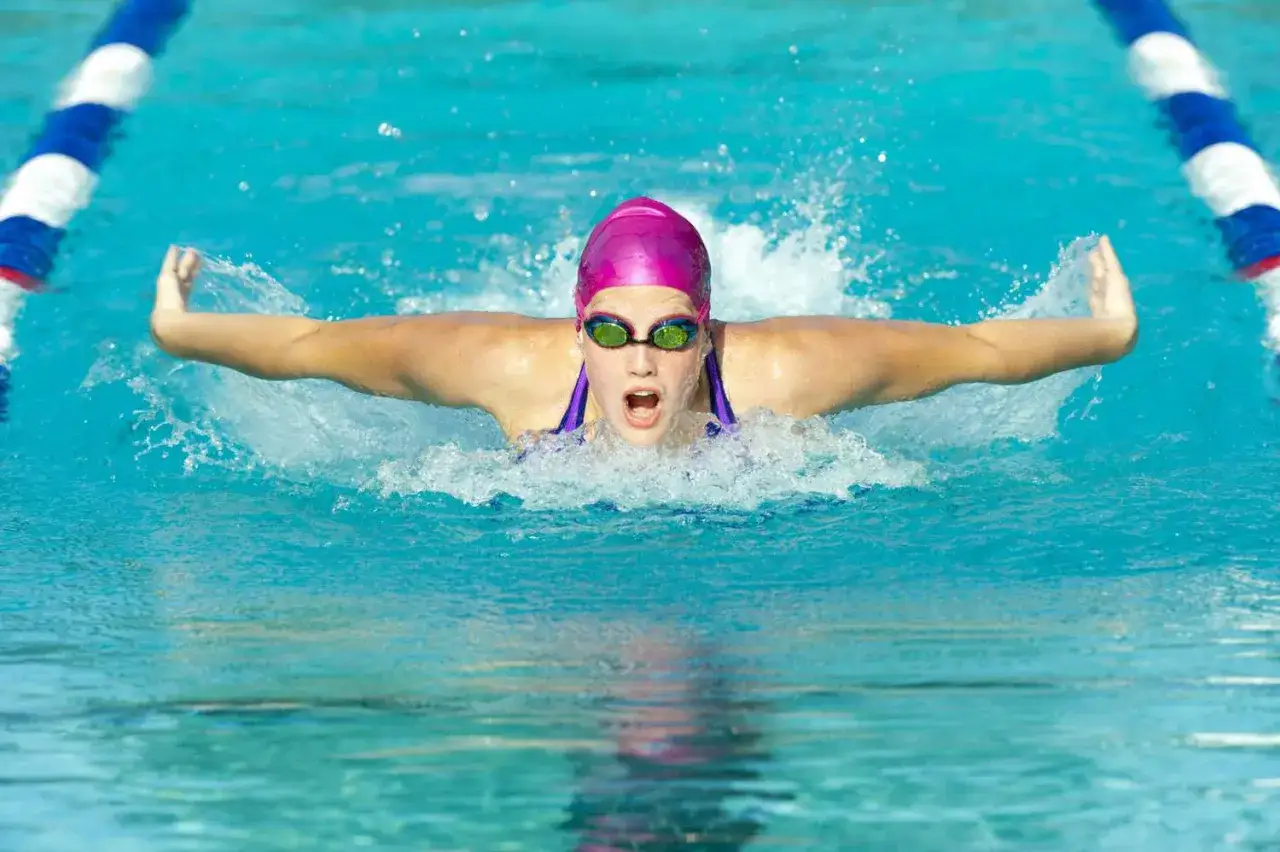 A young swimmer practices butterfly stroke, a challenging technique learned in swim stroke lessons, with arms extended and water splashing.