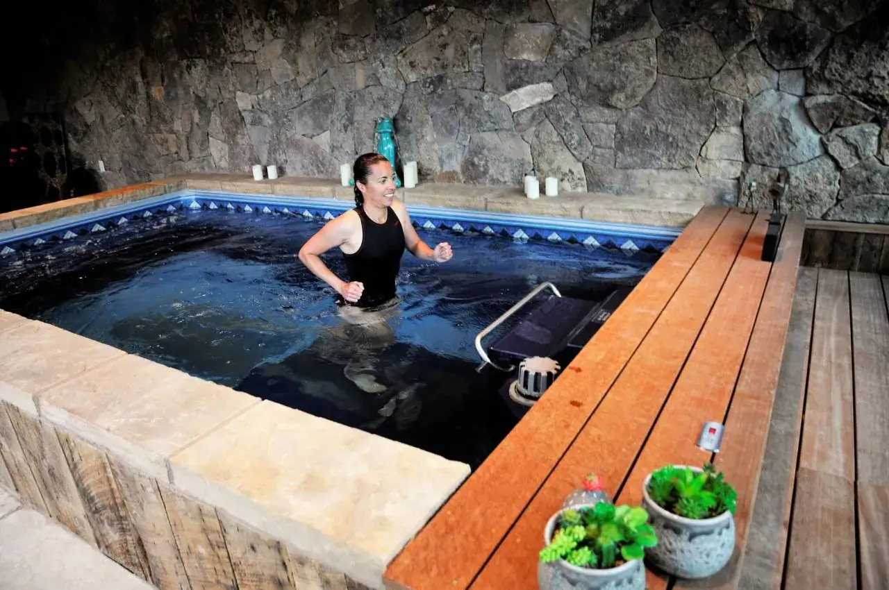 Woman running in an underwater treadmill, performing a challenging vo2 max workout in a serene, stone-walled pool area.