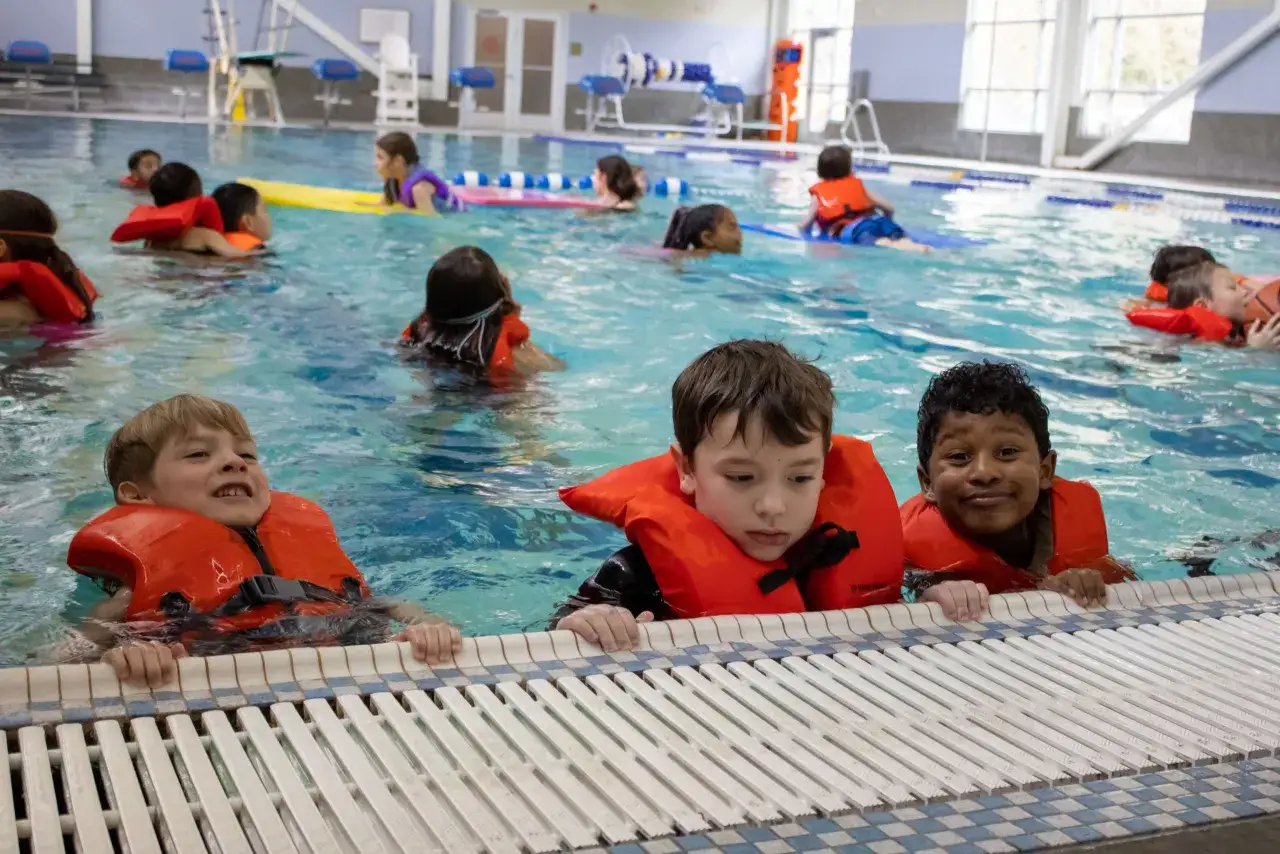 Children in orange life vests enjoy swim classes for 5 year olds, splashing and learning in the pool.