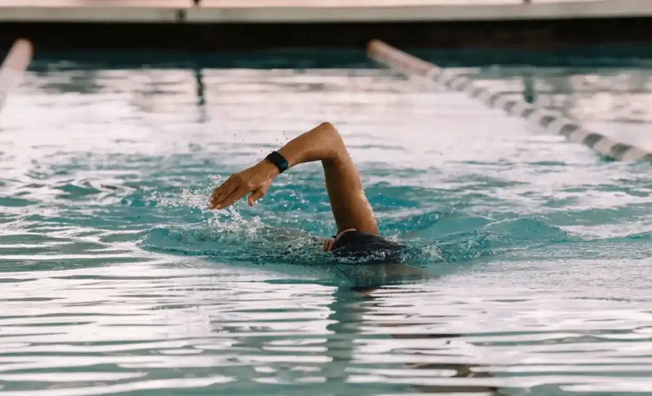 Swimmer's arm emerges from blue water, a fitness tracker on their wrist. This workout intensity is like asking 
