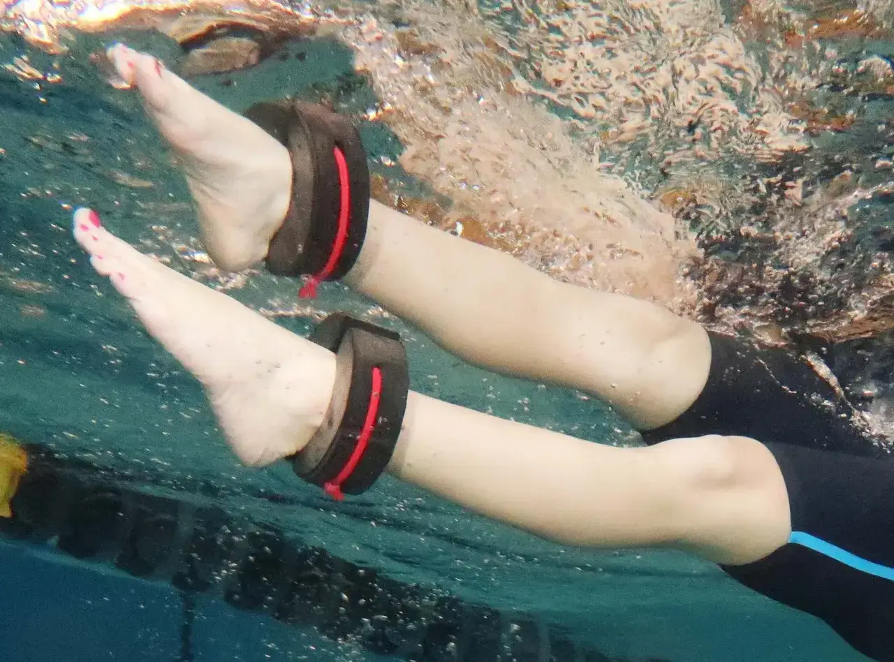 Underwater view of legs with ankle weights, suggesting it's possible to swim with a sprained ankle for therapy.