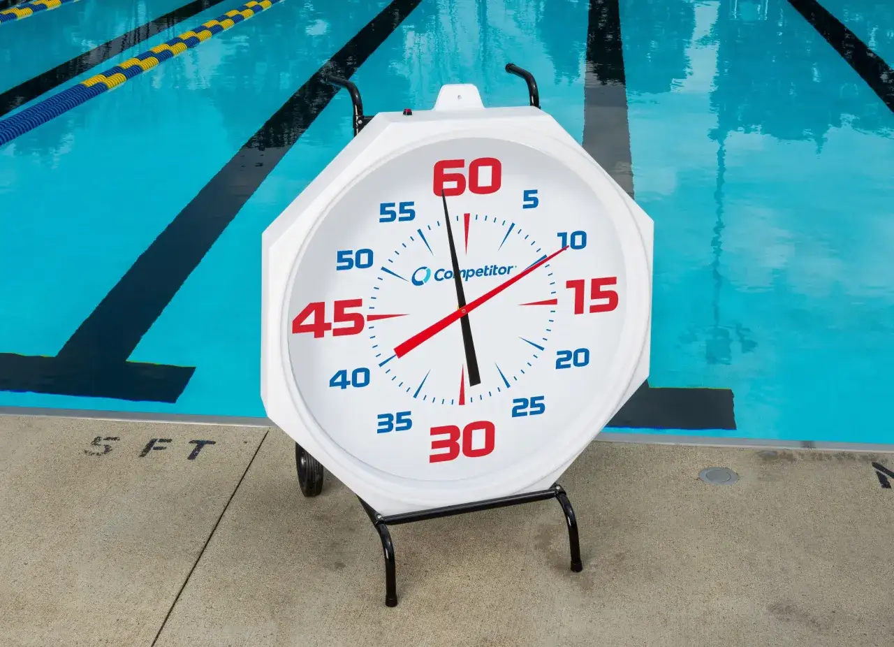 A large white stopwatch sits poolside next to a triathlon pool, ready to time the next race.