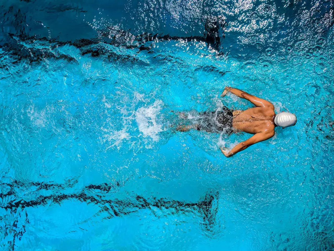 A swimmer in a white cap powers through the water, a testament to dedicated swim conditioning.