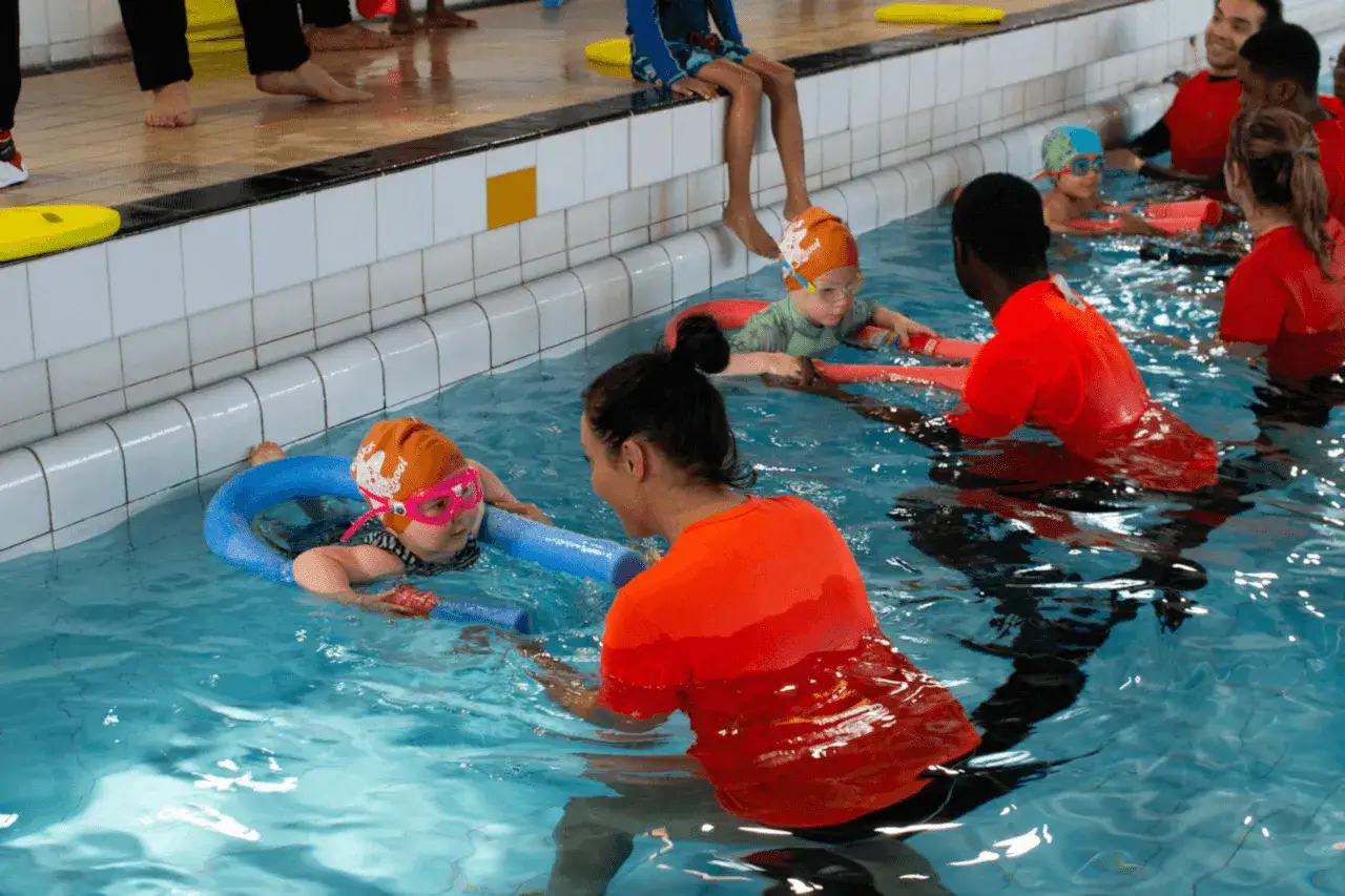 A swim instructor helps a child with a noodle in a pool. This scene highlights the rewarding nature of swim instructor jobs.