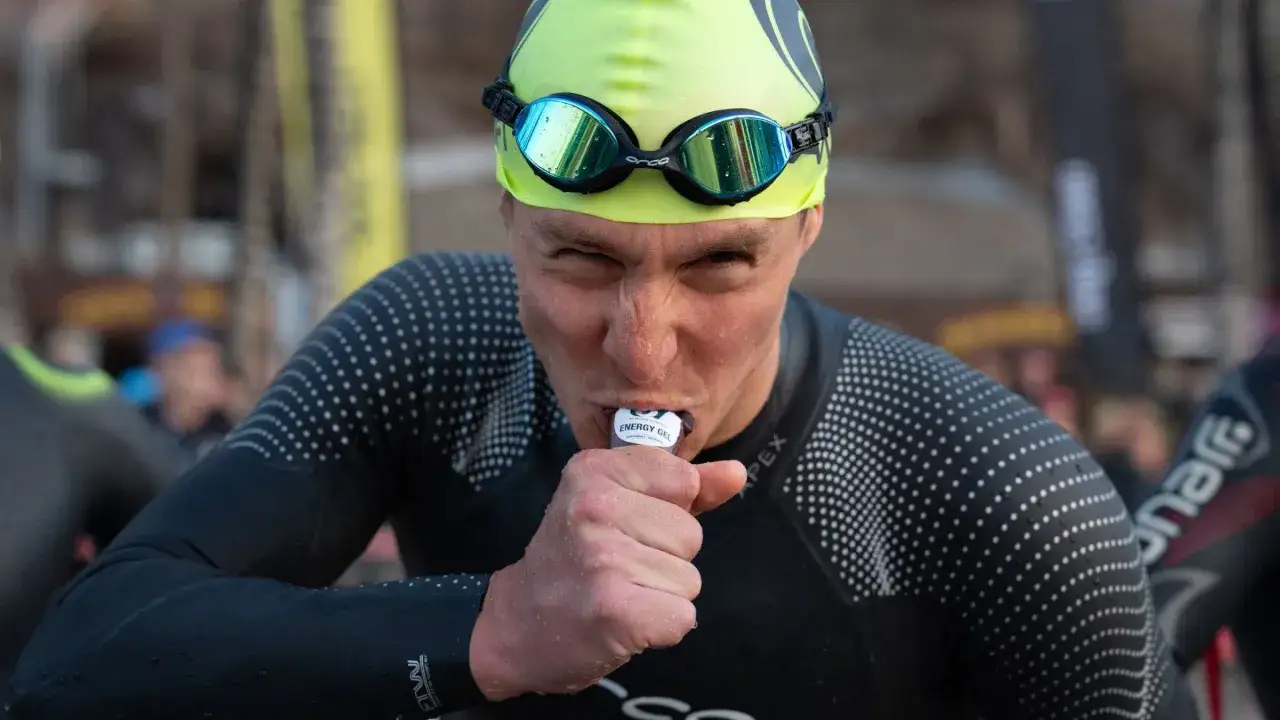 Triathlete Jesse Thomas, wearing a neon cap and goggles, takes an energy gel during a race.