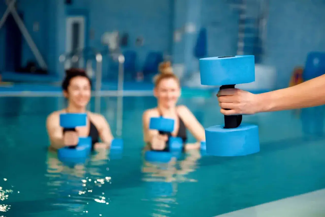 Women enjoying water aerobics with blue dumbbells. A great workout before and after a long day.
