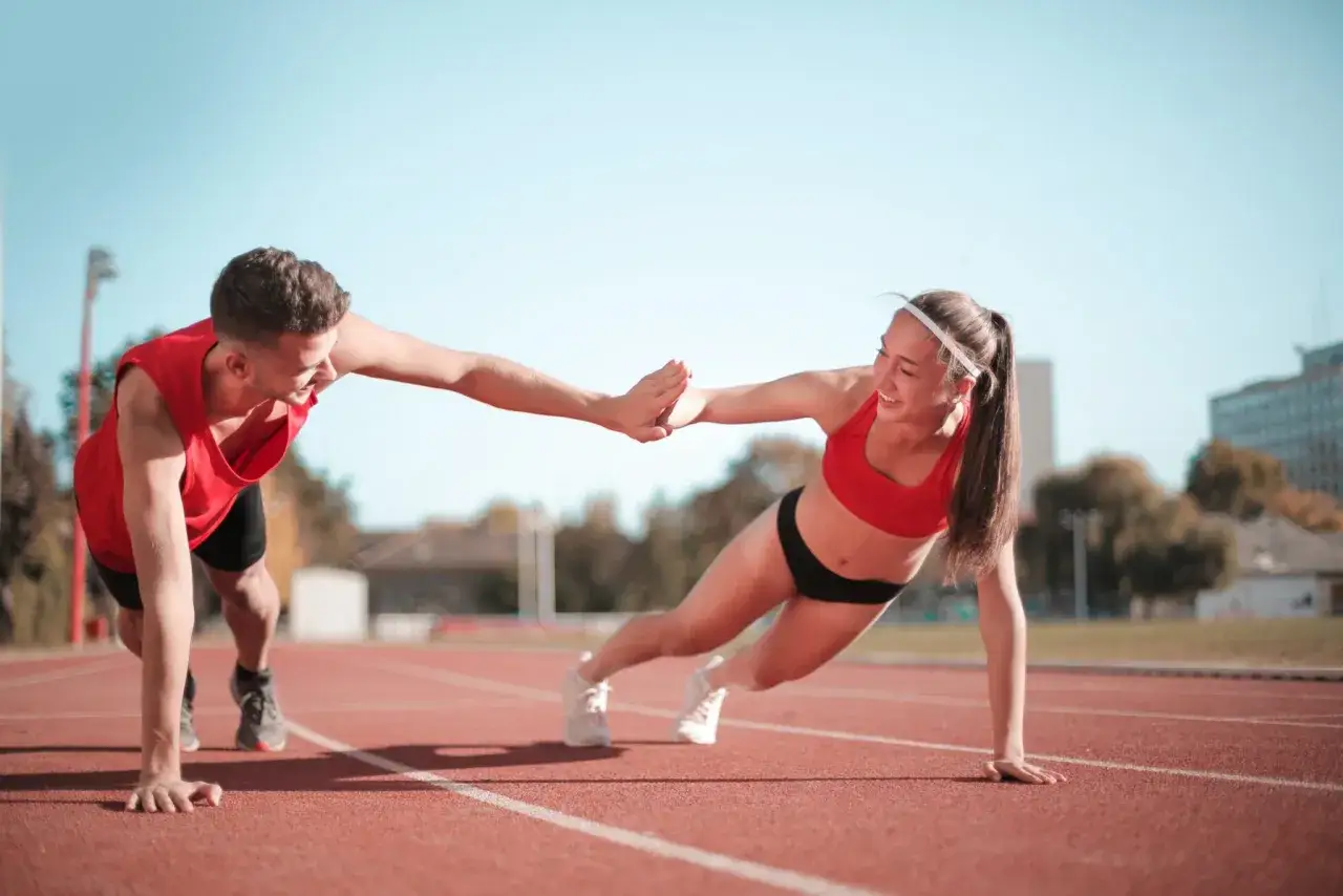 Two athletes high-five while doing push-ups on a track, showcasing their dedication to swimmers exercise.