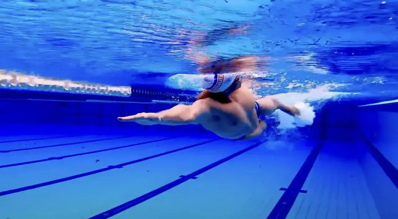 Underwater view of a swimmer performing the combat sidestroke in a blue pool.