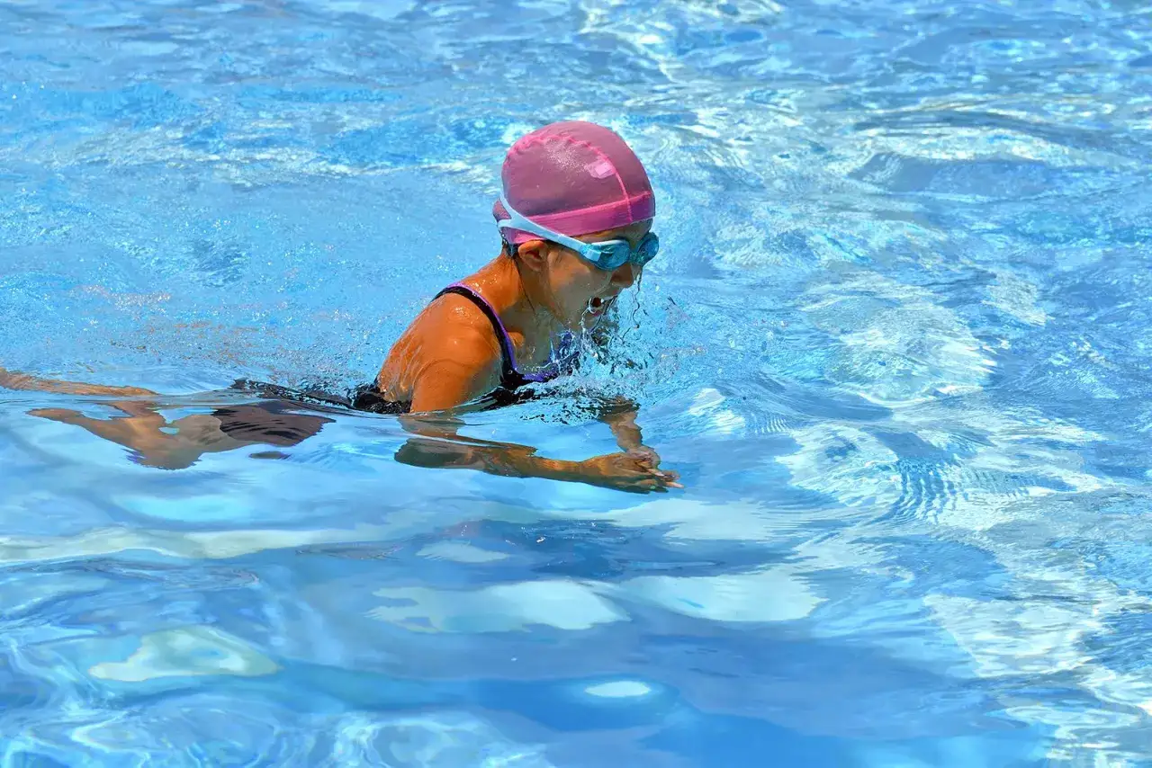 A young swimmer in a pink cap and goggles practices breaststroke, enjoying the full-body workout and cardiovascular breaststroke benefits.