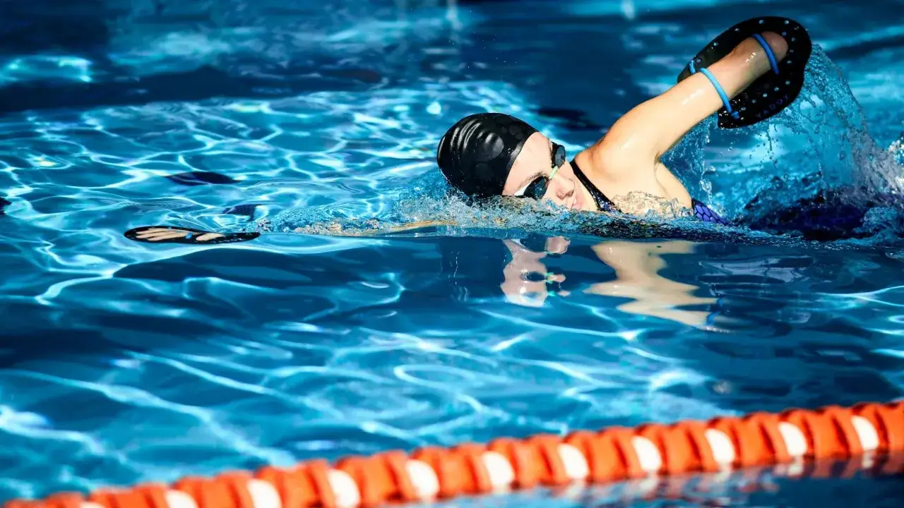 Swimmer with hand paddles, executing a stroke as part of a rigorous swim workout plan.