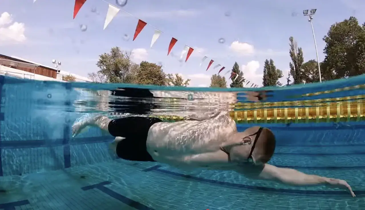 A swimmer performs a side stroke swim in a pool, with red and white flags strung overhead.