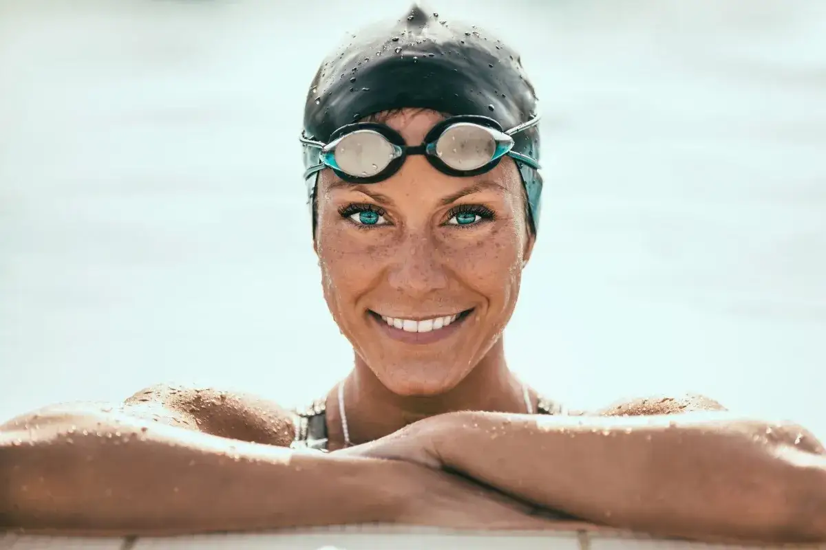 A swimmer with bright blue eyes and a cap smiles, ready to dive in. She's proof you can wear contacts in the pool!