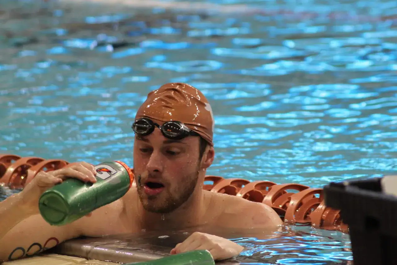 Swimmer with goggles and cap drinks from a green bottle. He's in a pool, and you might wonder, do you sweat when you swim?