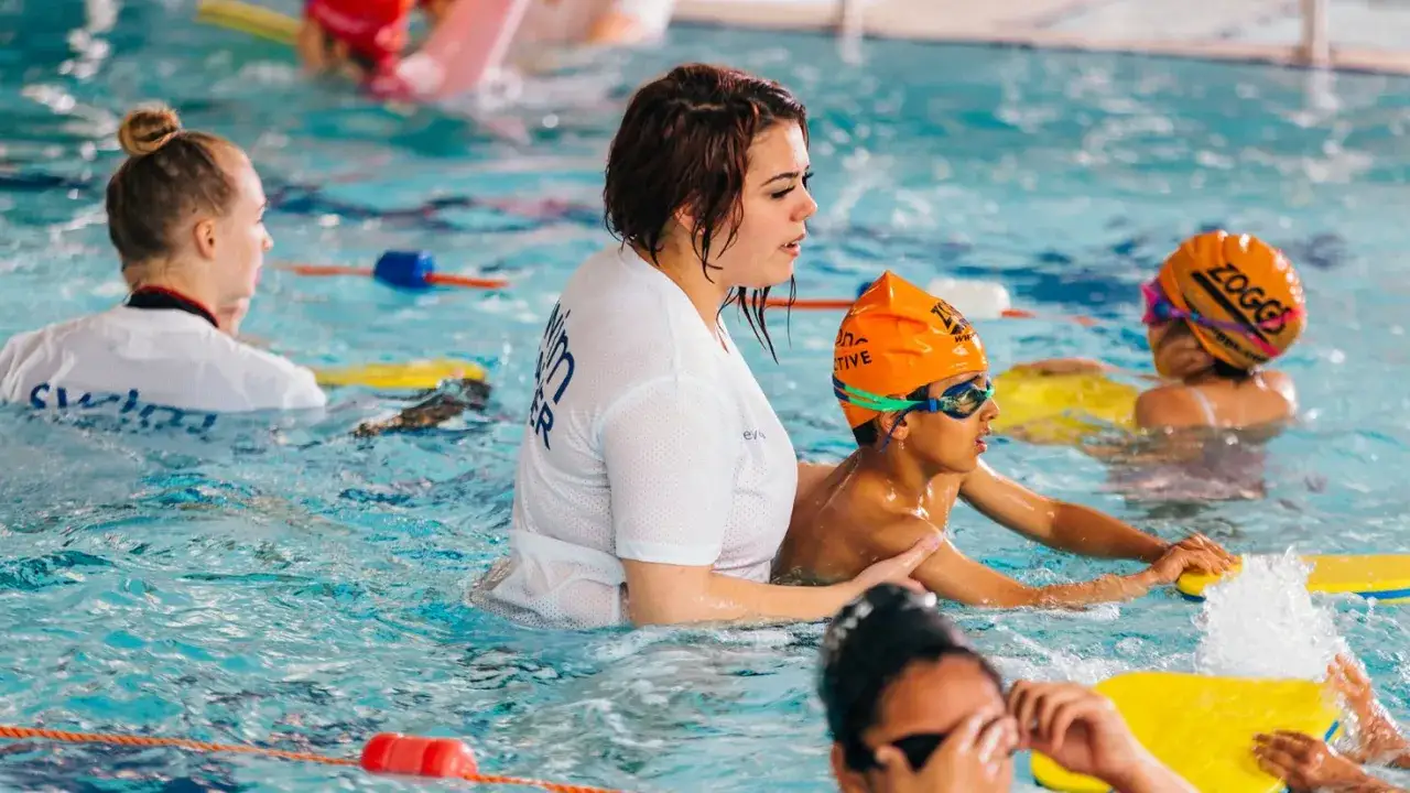 Swim instructor helps a child learn to swim, showing what age can a child swim independently.