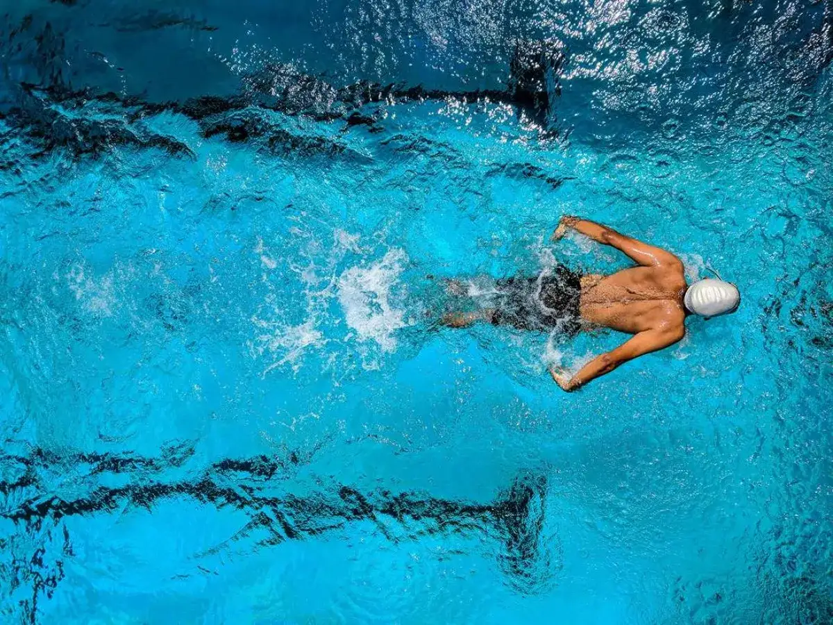 A swimmer glides through blue water, their body creating ripples. It's hard to tell how many swim strokes are there, but the motion is powerful.