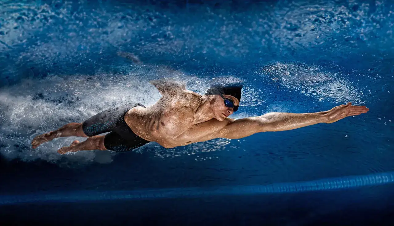 An athletic swimmer glides through the deep blue water, creating a powerful wake. The water crunches around his streamlined body as he propels himself forward.