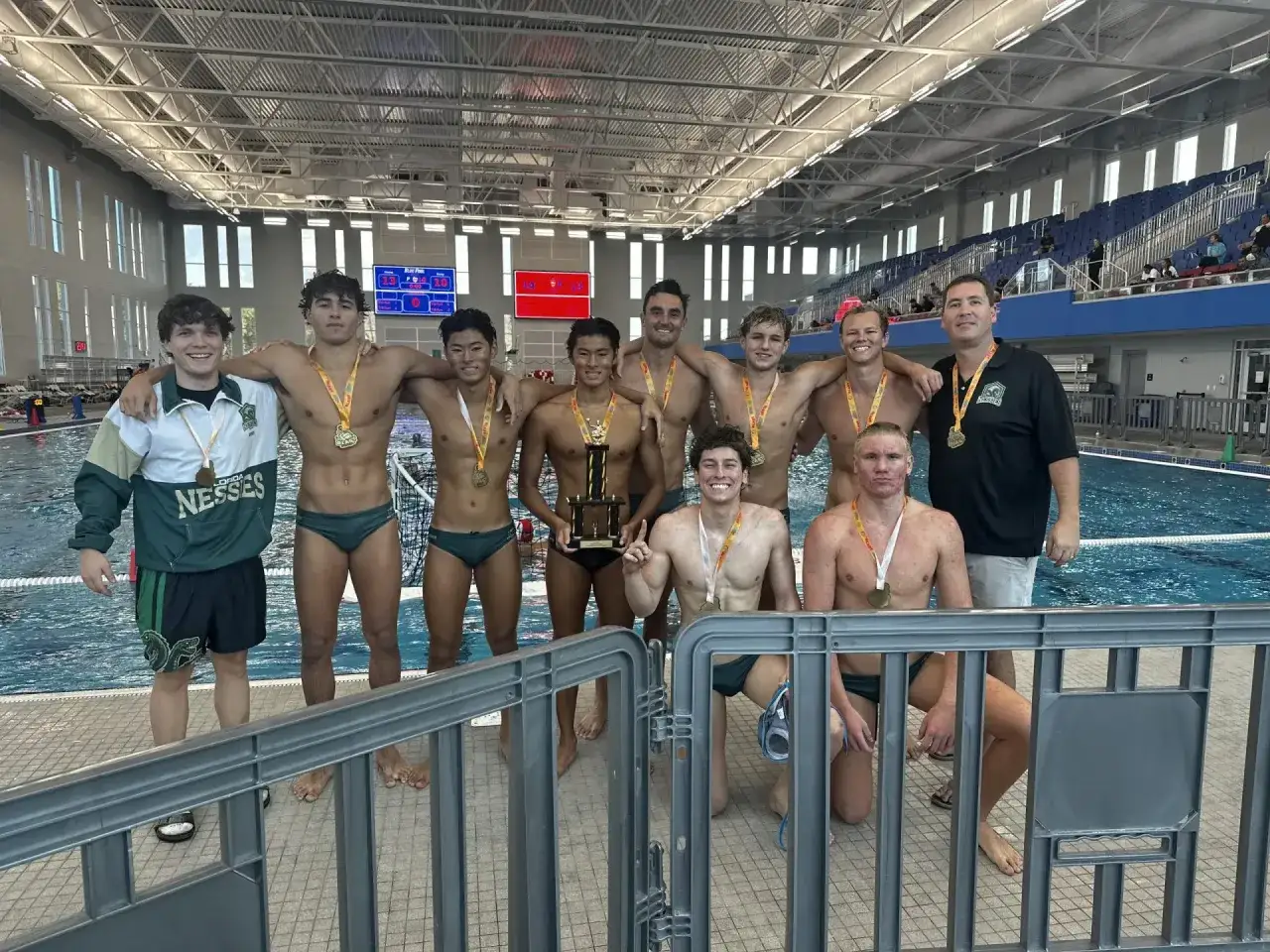 Proud water polo players, winners of a championship, pose with their trophy and medals in a pool facility.