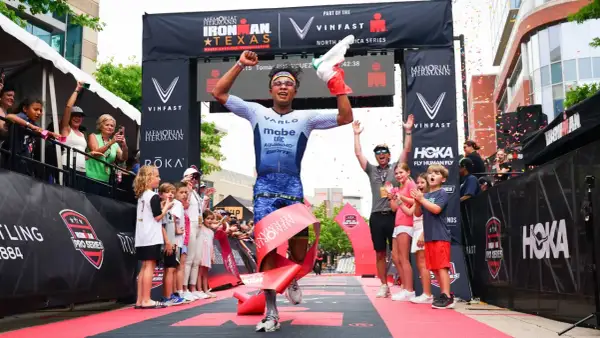 A triumphant athlete breaks the tape at the Memorial Hermann Ironman Texas, celebrating a victory in this demanding team triathlon event.