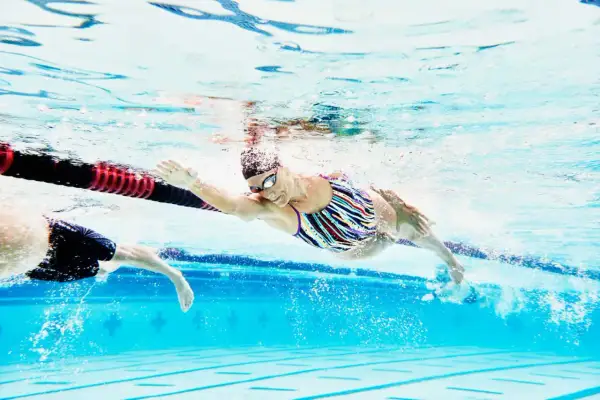 A swimmer in a colorful suit glides through the water, her arm extended, during a recovery swim workout.