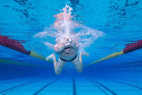 Underwater view of a man performing the breast stroke in a swimming pool, with lane lines and buoys visible.