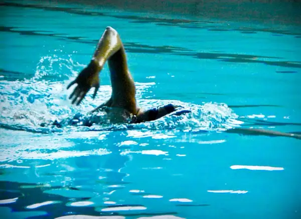 Swimmer's arm in a powerful high elbow catch, slicing through the turquoise water with a splash.