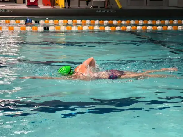 A swimmer in a green cap performs a front crawl swim, their body streamlined as they glide through the turquoise water.