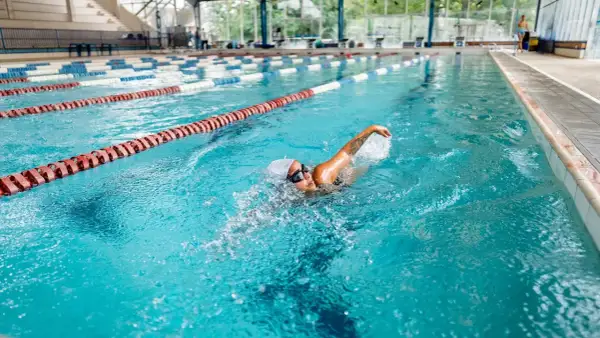 A woman enjoys a 30-minute pool workout, swimming laps in a bright blue lane.