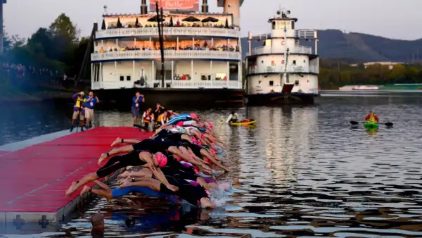 Triathletes dive into the water at 70.3 Chattanooga, with paddle boats and riverboats in the background.