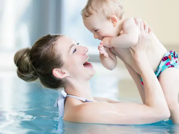 Mother and baby laughing in a pool. A happy mom asks, "When can you swim after C-section?