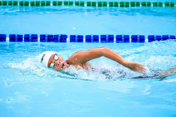Swimmer in a white cap and goggles executes a powerful american crawl stroke, churning the bright blue water.