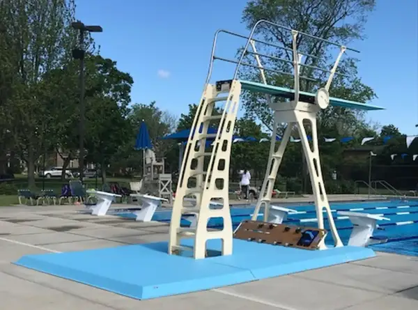 A tall, cream-colored high diving board stands ready for action next to a bright blue pool.