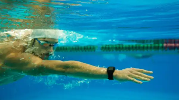 Underwater view of a swimmer in goggles and cap, focused on a long distance swim, with a smartwatch on their wrist tracking progress.