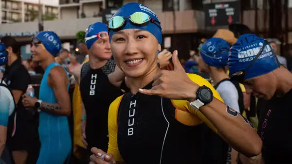 A smiling woman in a blue swim cap and yellow and black triathlon suit gives a shaka sign, ready for the honu triathlon.