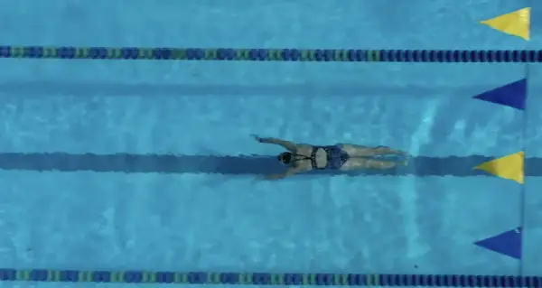 A swimmer glides through the water, executing a powerful breaststroke. The blue pool is marked with lane lines and colorful flags.
