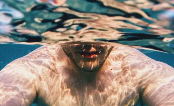 Underwater shot of a man's shoulders and mouth, with light patterns on his skin. A visual guide on how to breathe underwater for beginners.