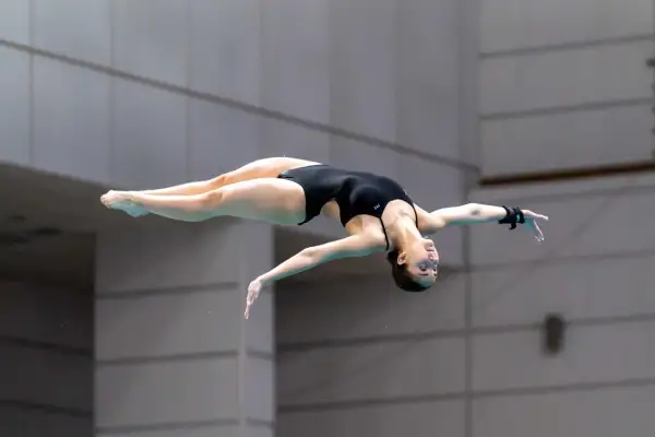 A diver executes a perfect pike position mid-air, body bent at the hips with legs straight and together.