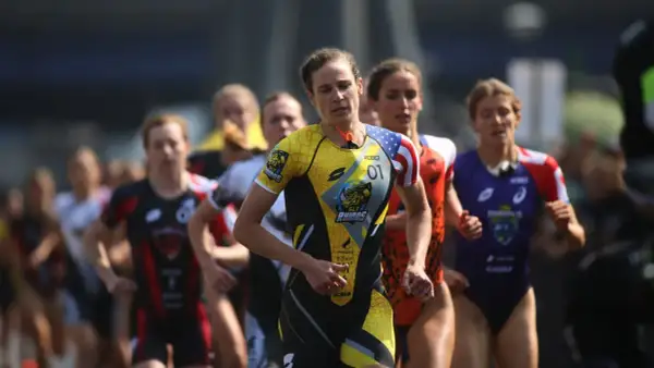 Katie Zaferes, number 01, leads a pack of triathletes in a race, her yellow and black suit featuring a rhino logo.