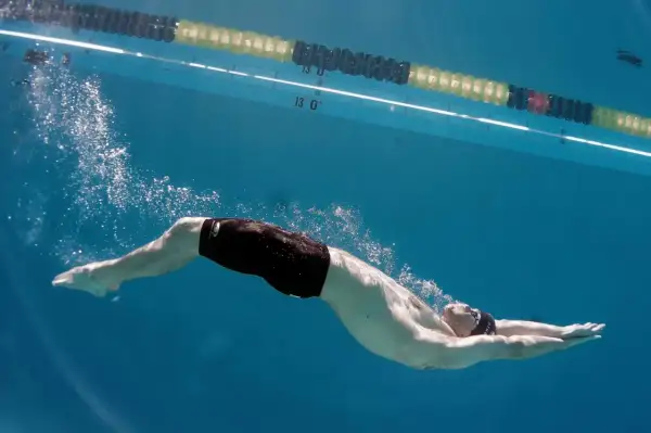 Underwater view of a swimmer performing a powerful kick, showcasing effective leg workouts for swimmers. Bubbles trail behind as they glide through the blue water.