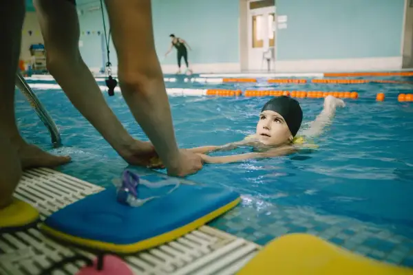 A child learns to swim with an instructor's help, experiencing the benefits of water safety and physical activity.